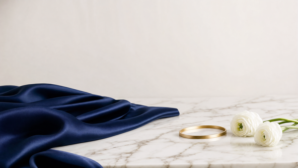 Seda azul-marinho, fio dourado e flores brancas sobre mármore — identidade premium Eternità