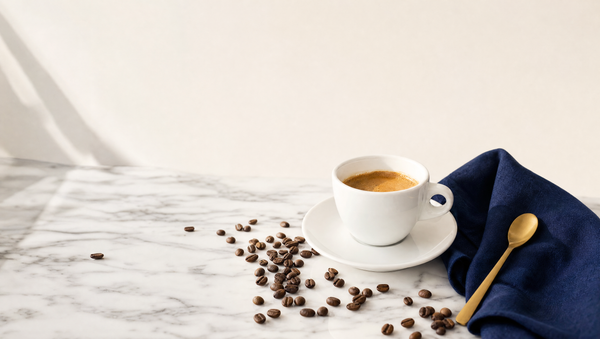 Xícara de espresso com grãos de café, guardanapo azul-marinho e colher dourada sobre mármore